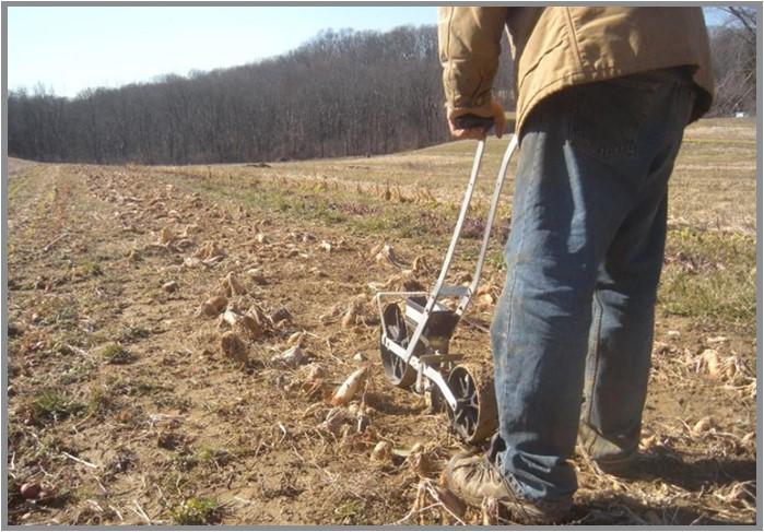 A farmer is using a push seeder in field.