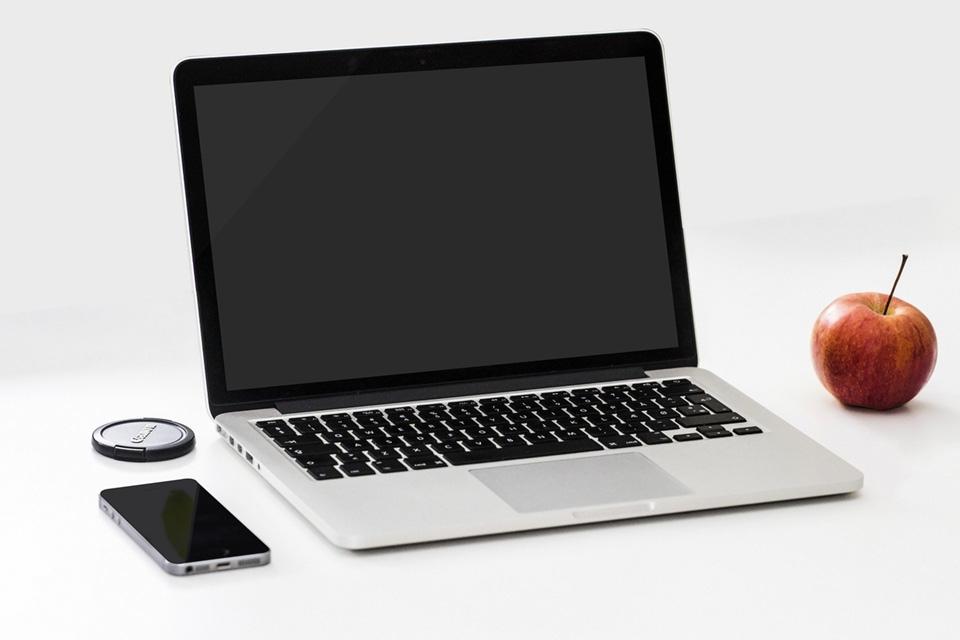 Laptop computer with a cell phone laying on the left side and an apple on the right.