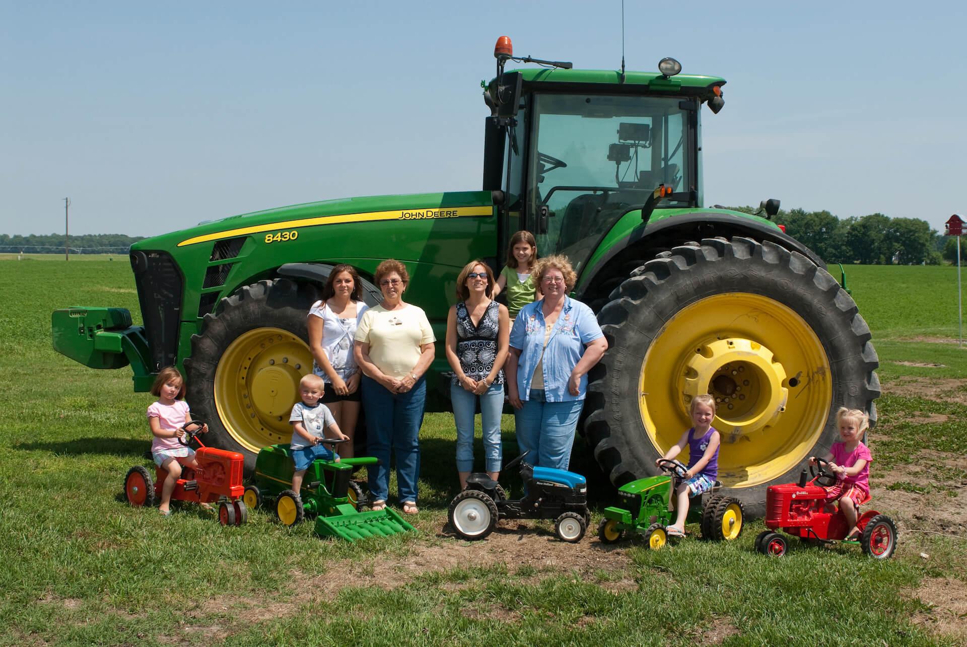 Four farm women standing in front of a tractor with their children