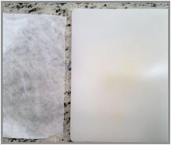 A damp paper towel next to a plastic cutting board. The cutting board will lay on top of the damp paper towel. The damp paper towel will prevent the cutting board from sliding out.