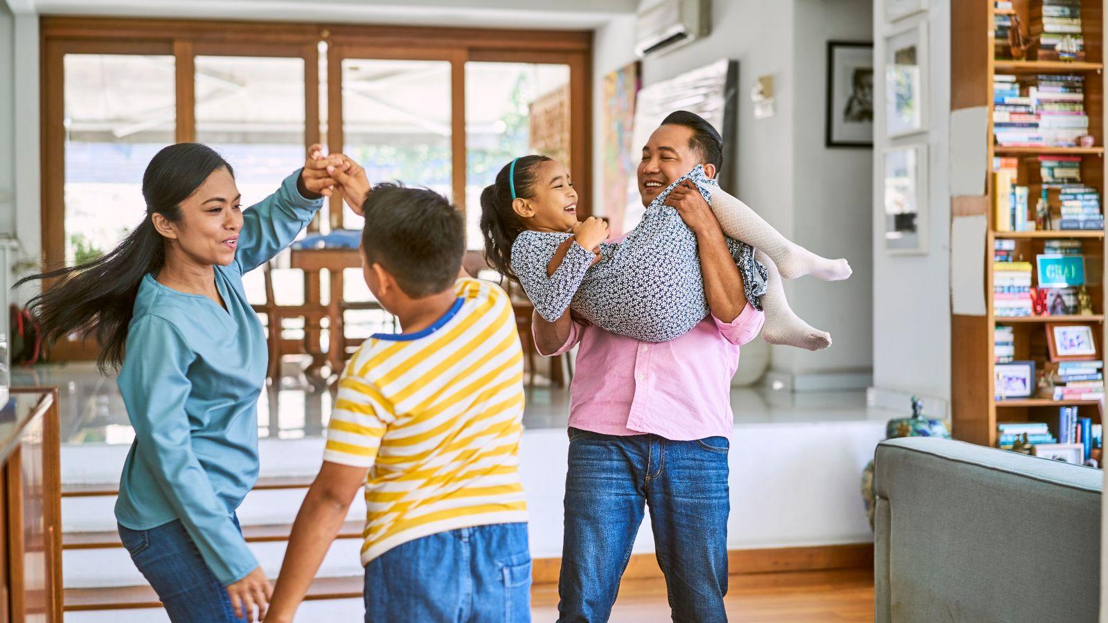 A multicultural family dancing in the living room. The father is holding the daughter.