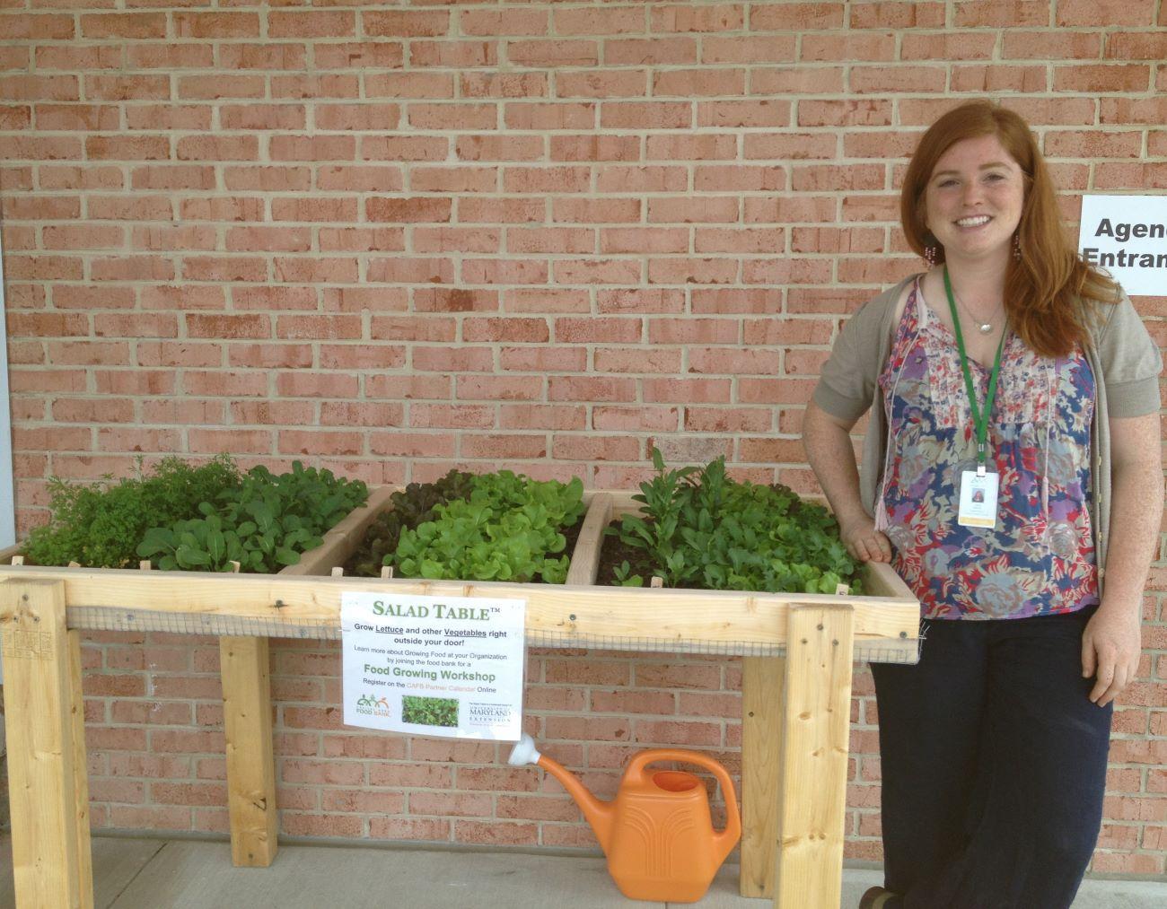 a woman standing next to a salad table planted with lettuces