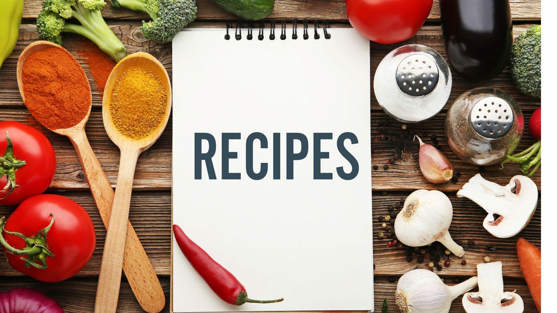 The word recipe on a notepad surrounded by spoons filled with herbs and cut up vegetables on a wood background