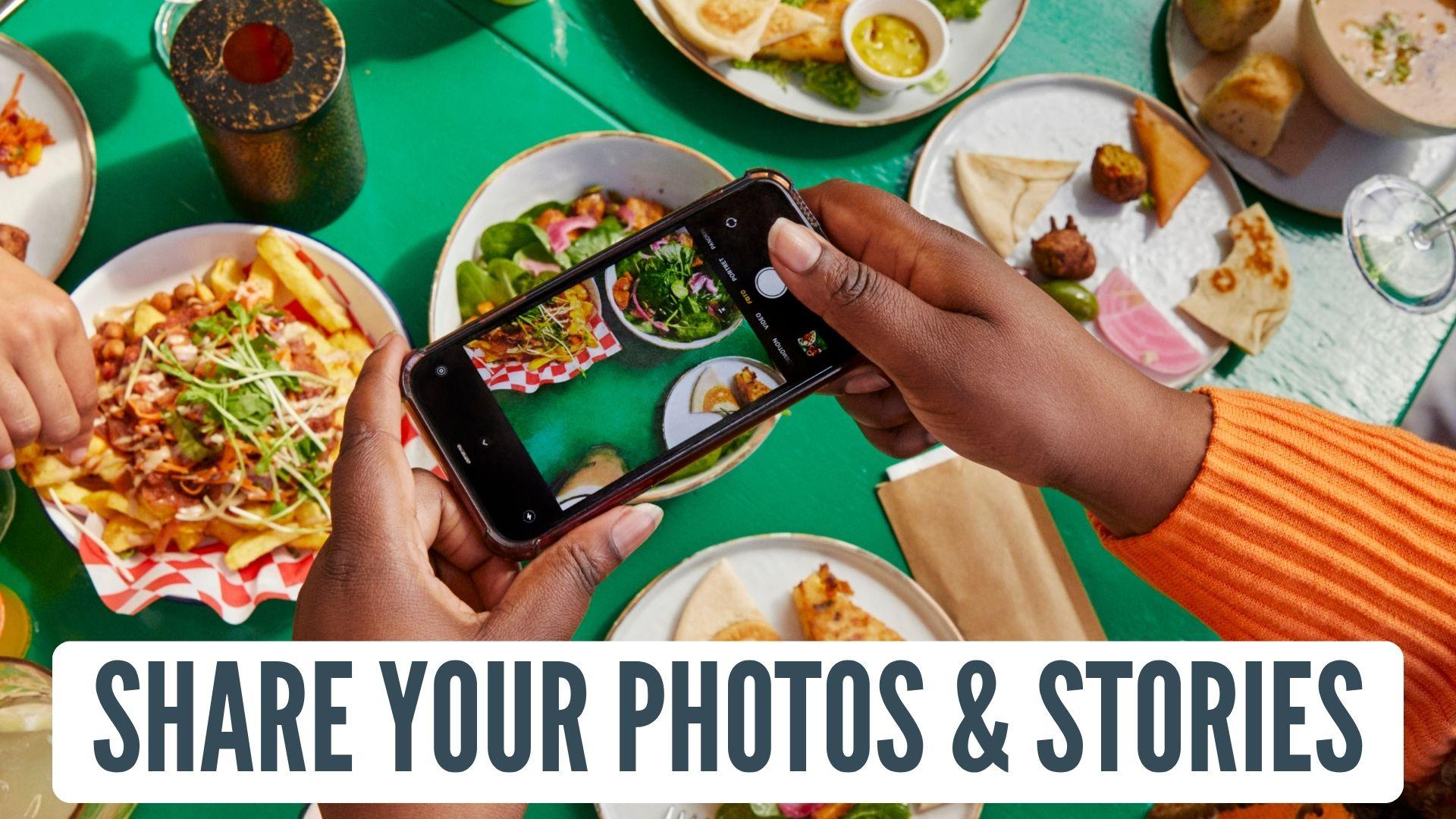 Share your photos and stories label on top of a table filled with food and a woman taking a picture of food on her cell phone