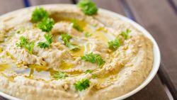 Bowl of baba ghanoush with parsley on top sitting on a table