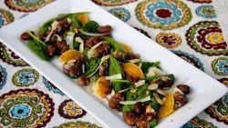 Fava bean salad with clementines on a white rectangular plate on a tablecloth with decorative circles