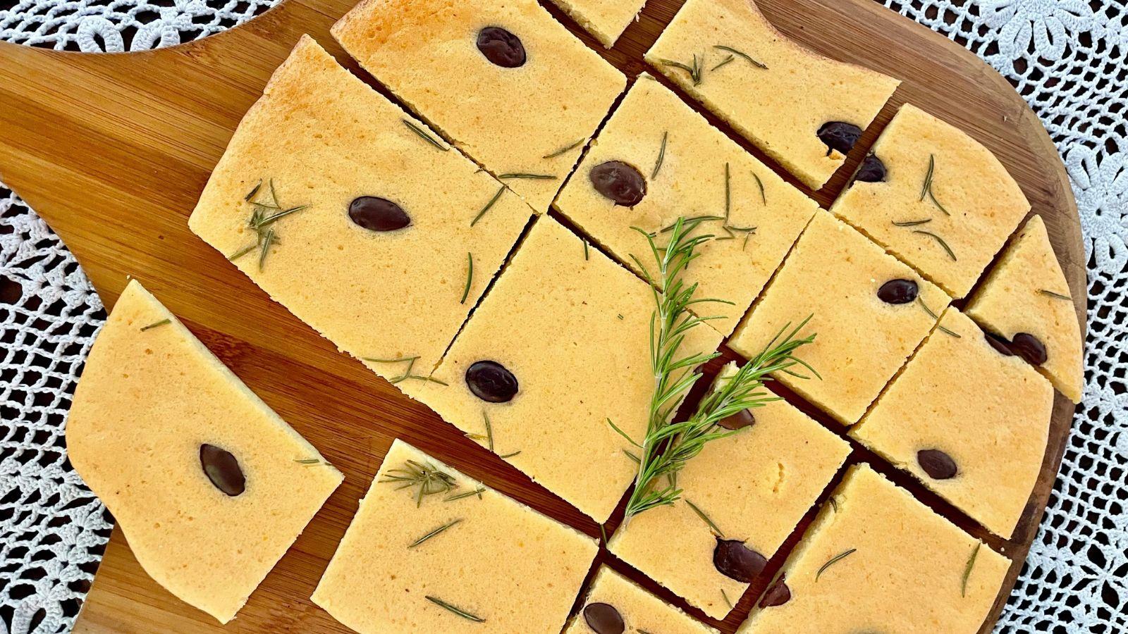 Red Lentil flatbread with rosemary and olives on top of a wooden paddle on a table