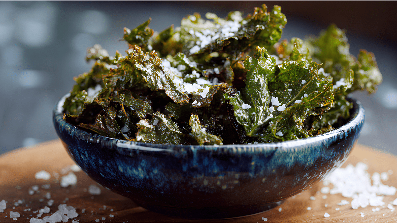 Crispy Baked Kale Chips laying in a blue bowl on a table with salt sprinkled