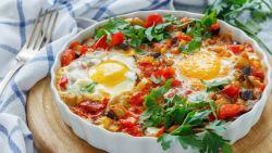White bowl filled with shakshuka sitting on a board next to a plate and napkin