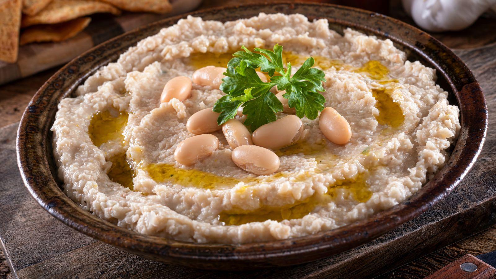 bowl of white bean dip with cannellini beans and parsley on top, on a wooden table