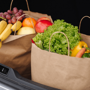 A brown grocery bag with parsley, carrots, and bell peppers sticking out of the top.