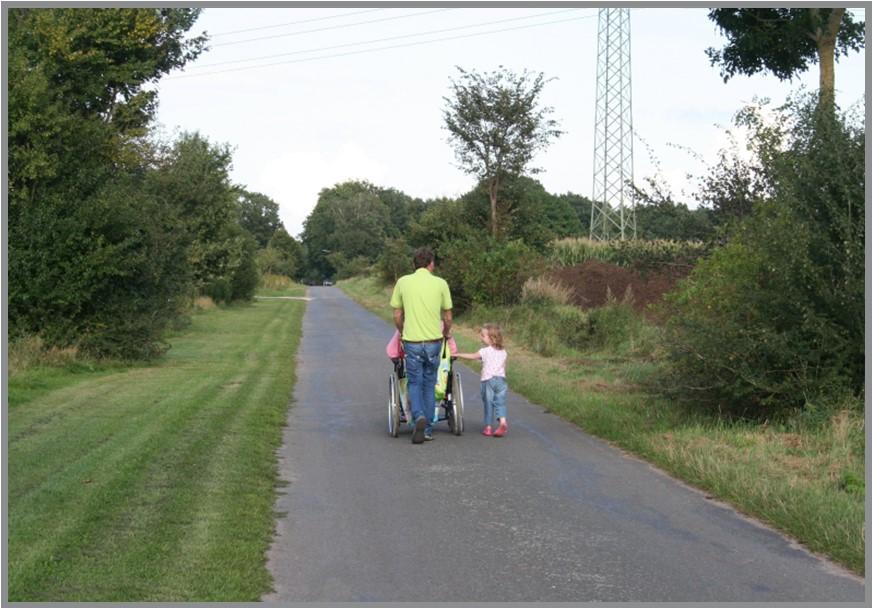 The family strolls down the driveway, gently guiding a wheelchair along with them.