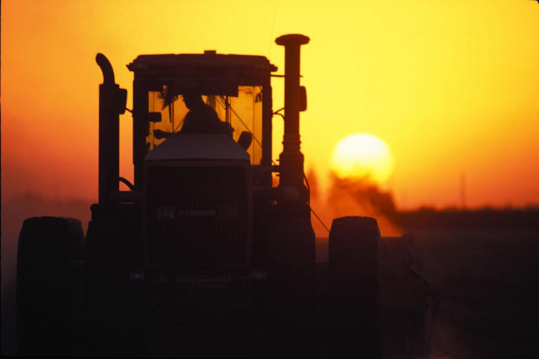 Farmer driving tractor with the sun setting in the background