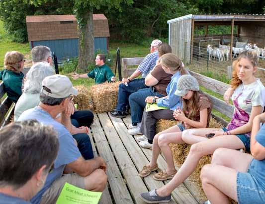 Men, women, and children are sitting on hay bales in a wagon farm tour. 