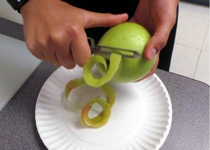 A person pealing a green apple