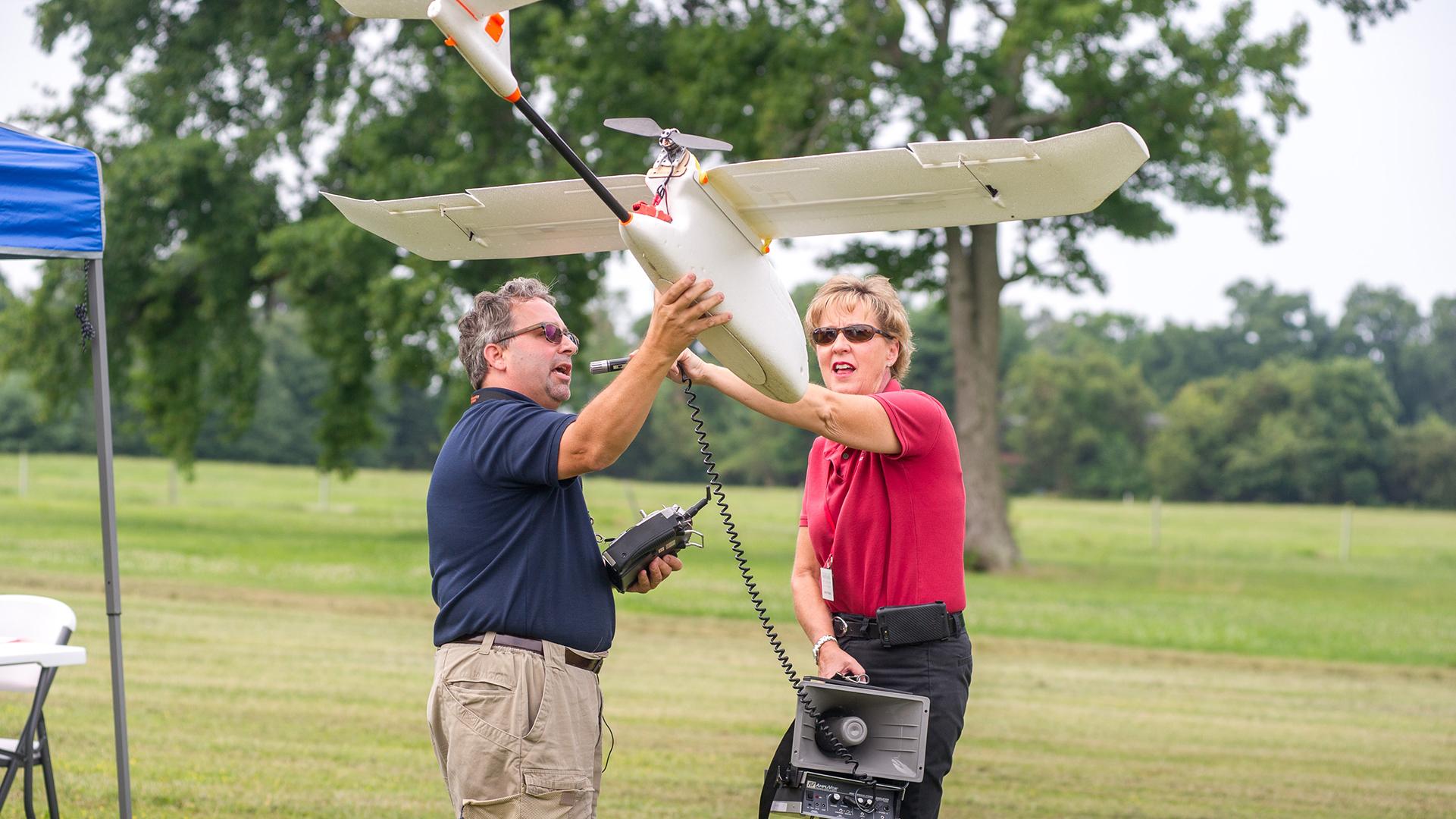 Two people holding up a precision ag equipment that looks like a small plane