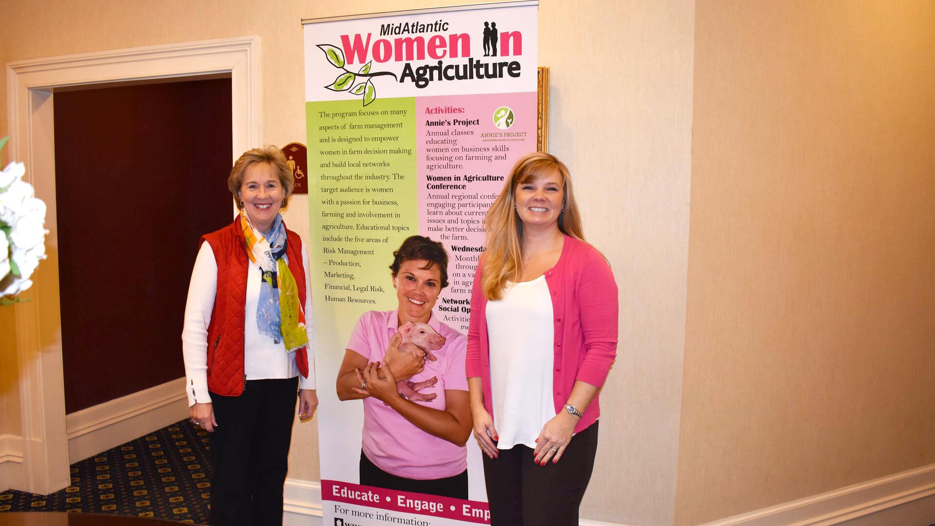 Two extension agents, Jenny Rhodes and Shannon Dill, standing in front of a Women in Agriculture sign