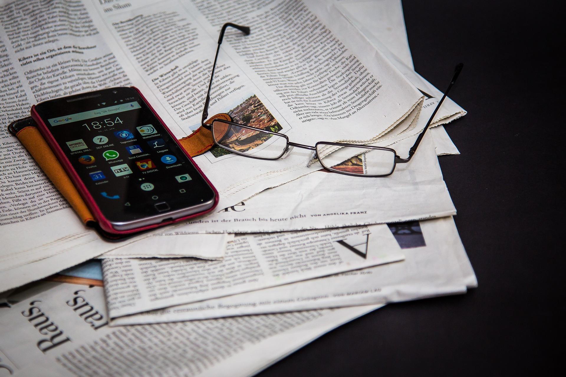 newspapers reading glasses and cell phone.