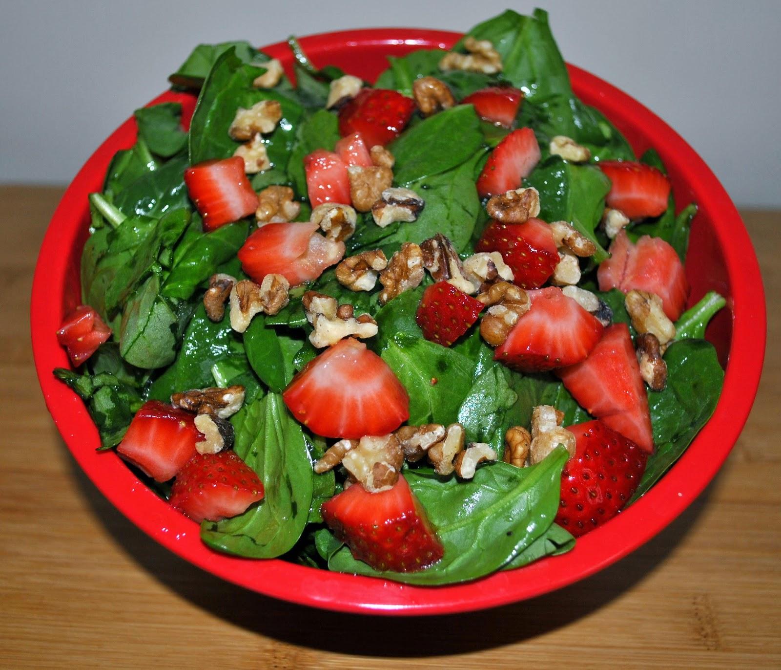 Spinach, strawberries and walnuts in a red bowl.