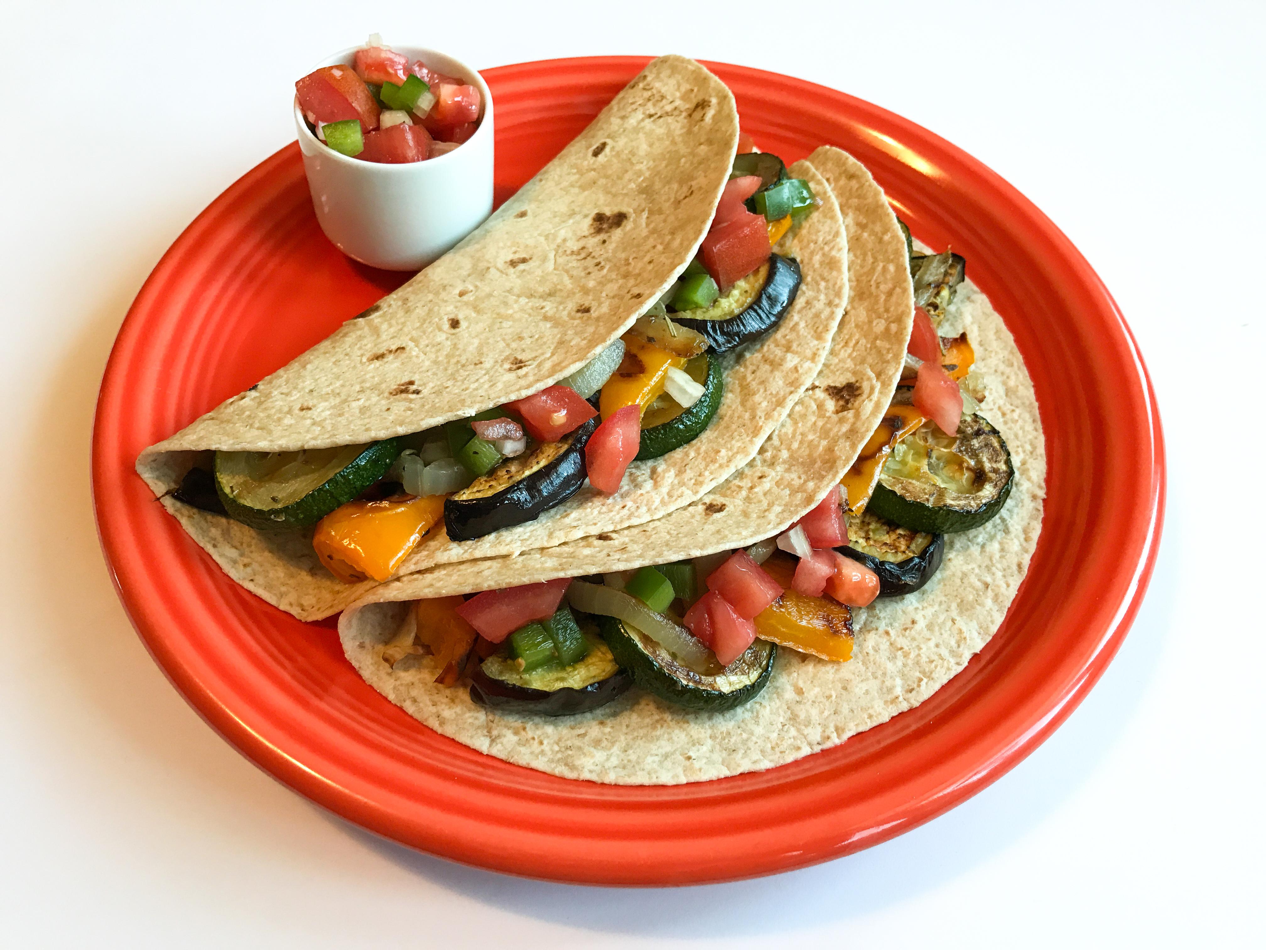 Two fajitas in a whole wheat tortilla with zucchini, bell peppers, and tomatoes served on an orange plate.