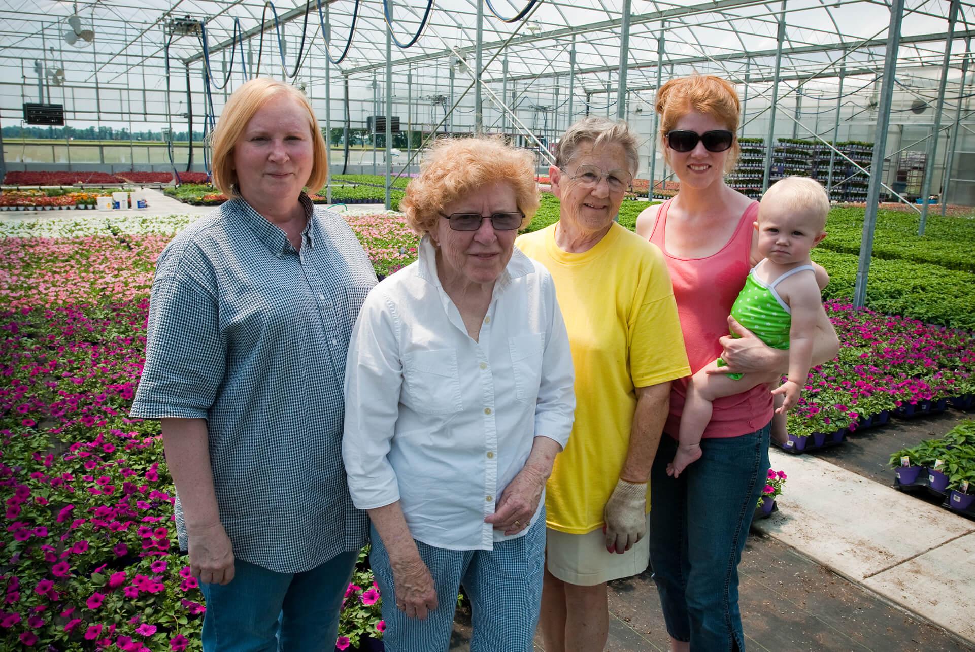 A generation of women farmers standing in a greenhouse filled with flowers