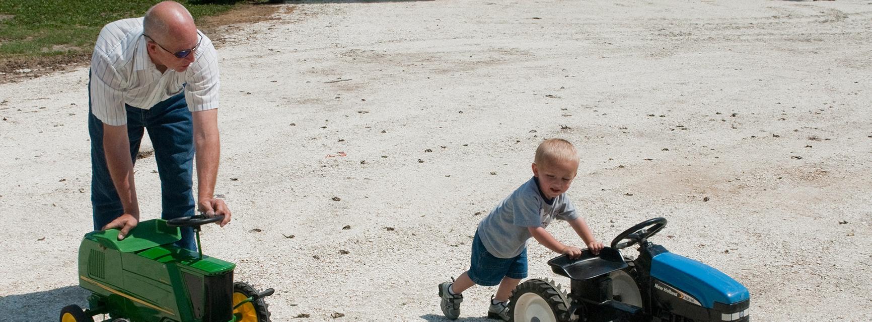 Father and son pushing small toy versions of farm equipment machinery