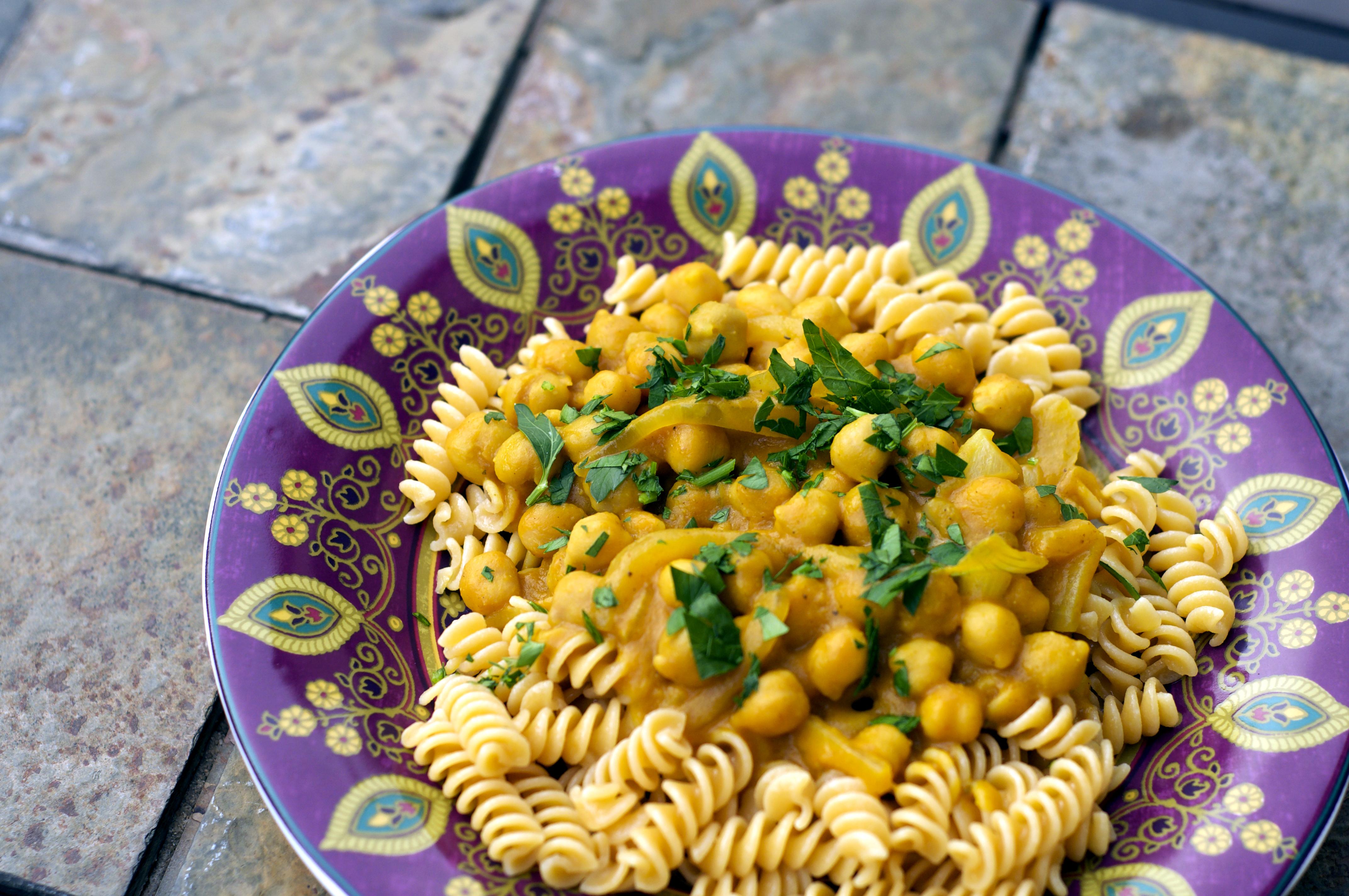 Pasta with pumpkin chickpea sauce and basil in a colorful purple bowl.