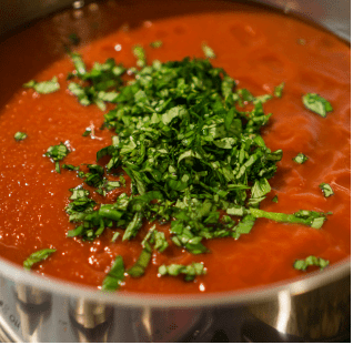 Tomato sauce topped with basil cooking in a pot.
