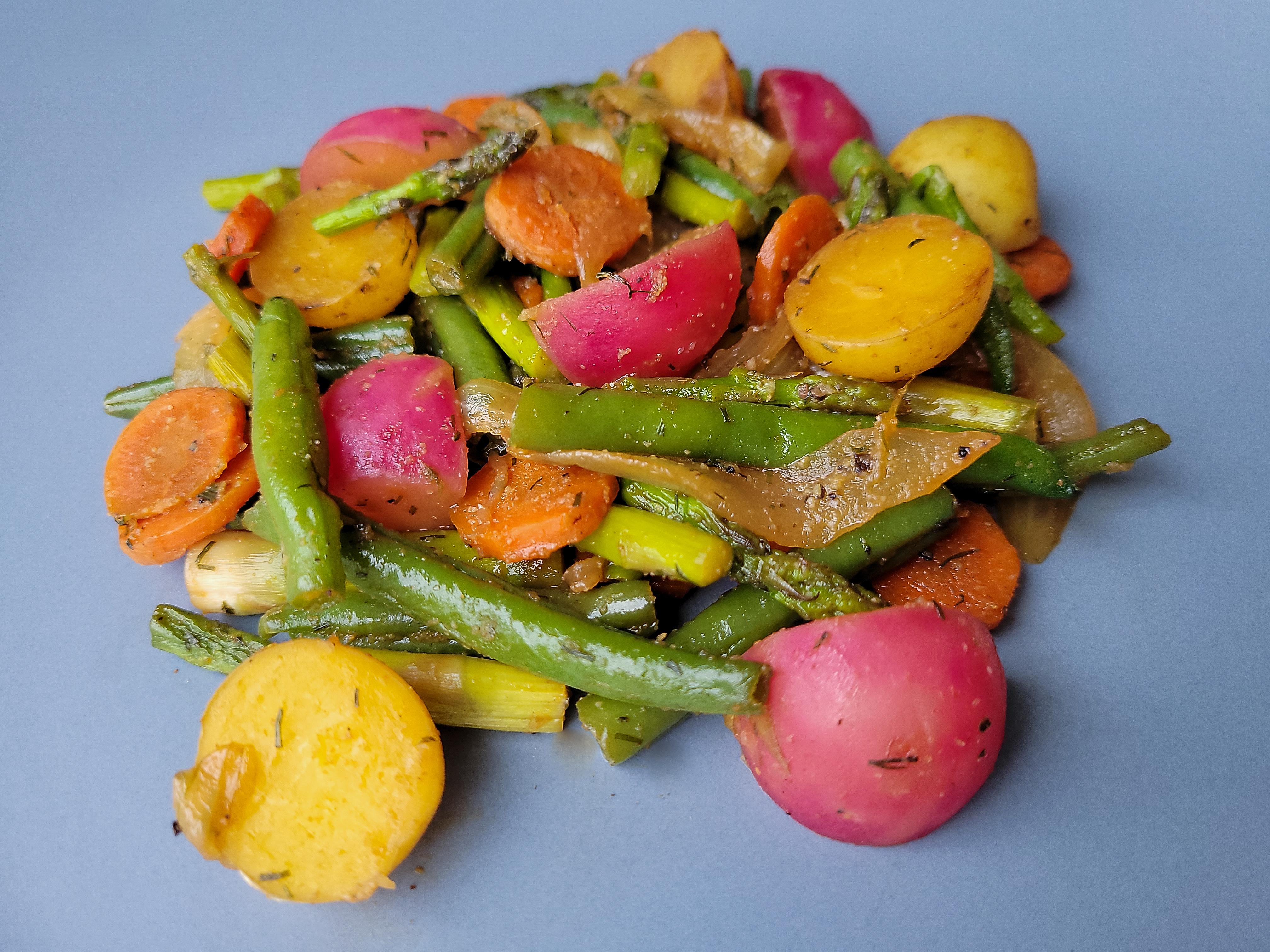 Spring vegetables including potatoes, carrots, asparagus, radishes and sugar snap peas on a blue plate.