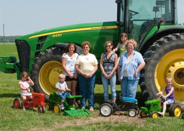 Farm women standing in front of a tractor and children sitting on thier toy farm equipment 