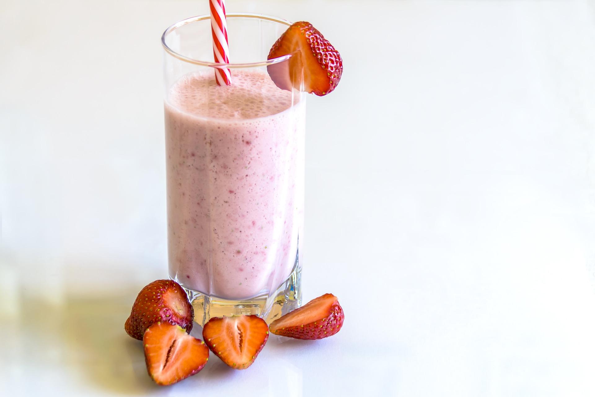 Strawberry smoothie in a large clear class with a red and white straw and garnished with strawberries around the glass.