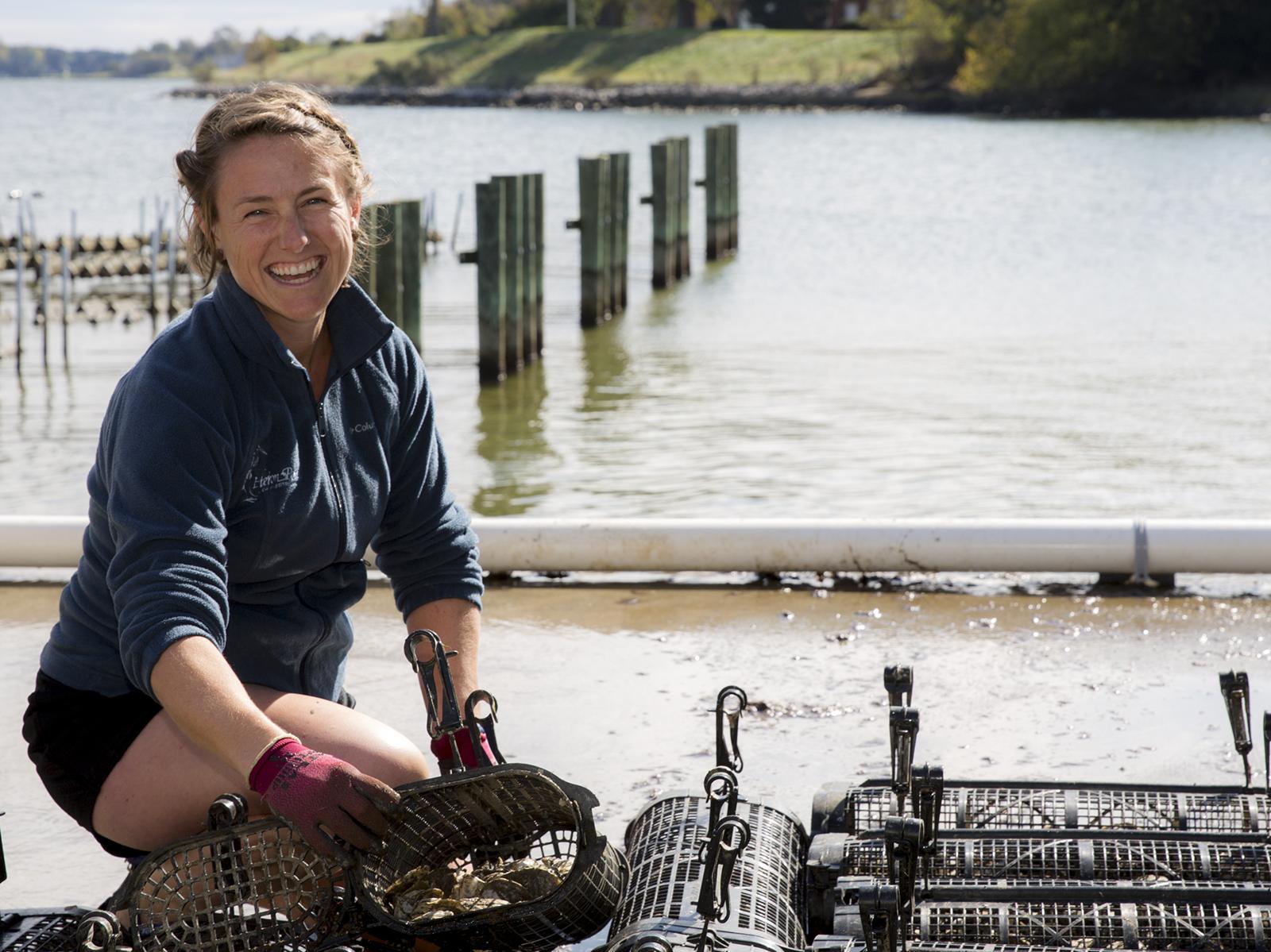 Photo of Shannon Hood kneeling beside oyster cages
