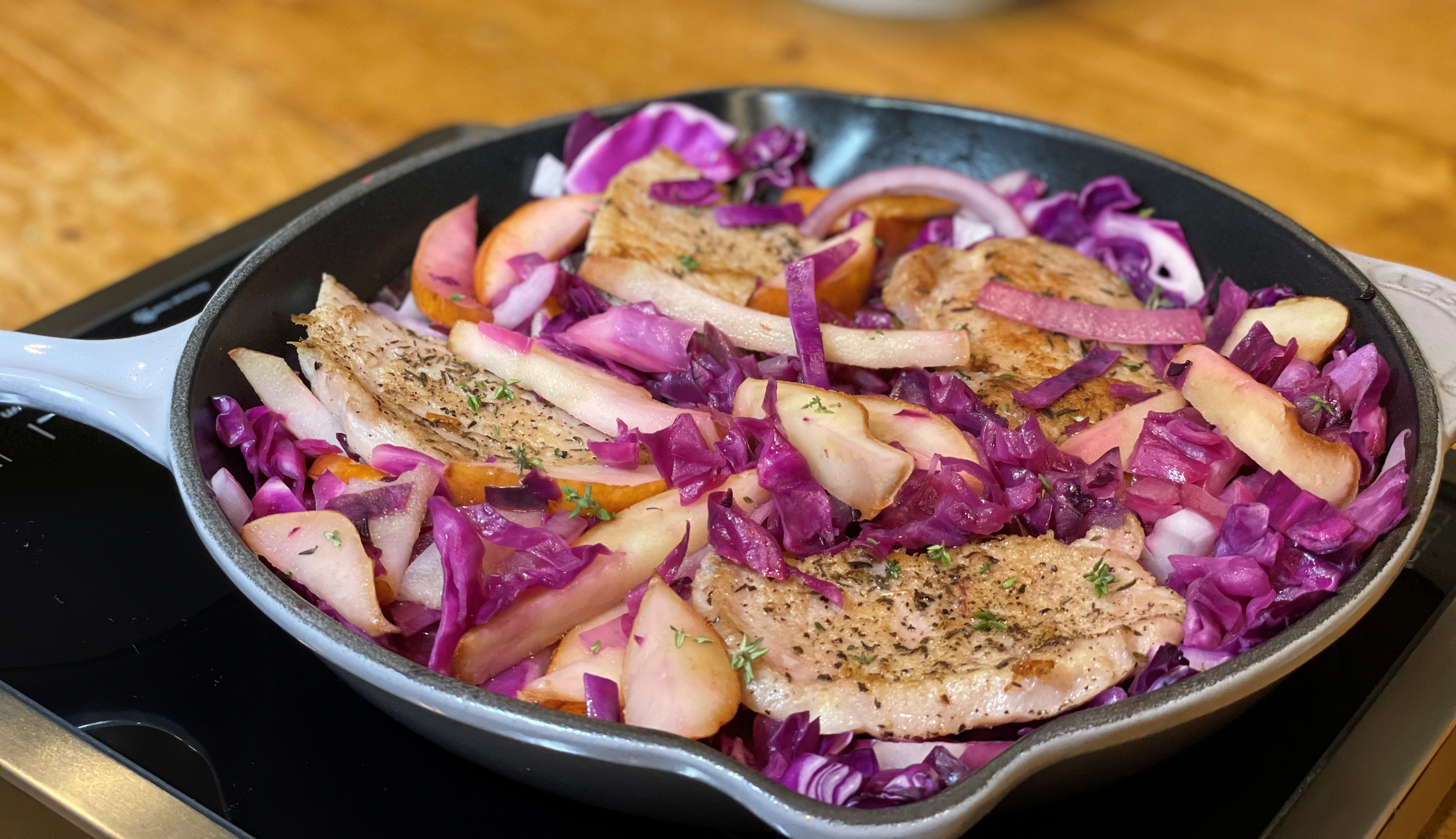 Pork chops, red cabbage and pears in a skillet sitting on a wooden table.