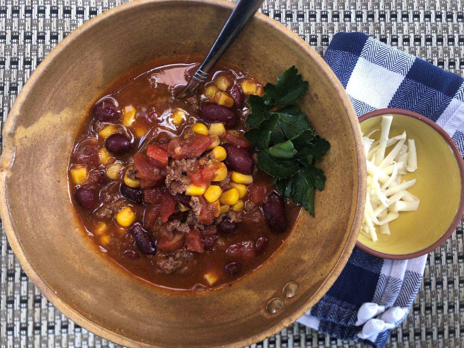 Taco Soup with kidney beans, ground beef, tomatoes and corn garnished with parsley and a bowl of mozzarella cheese to the right hand side.