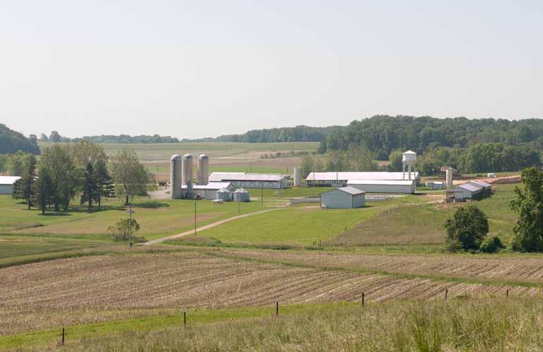 Farmland with farm buildings and silos in the background