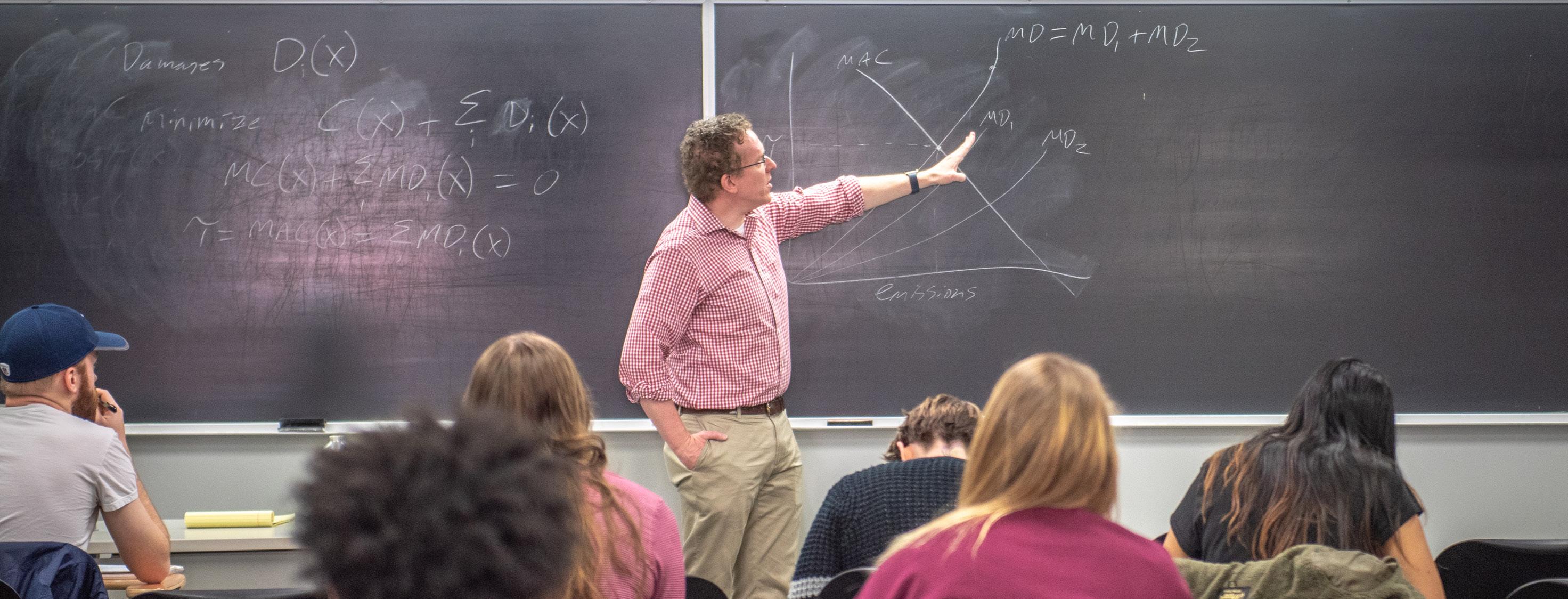 Instructor (man) pointing at a chalkboard