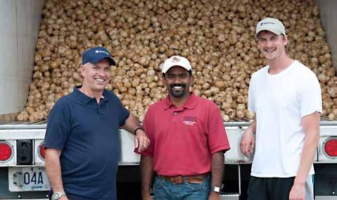 Three men standing at the back of a tractor-trailer filled with harvested potatoes