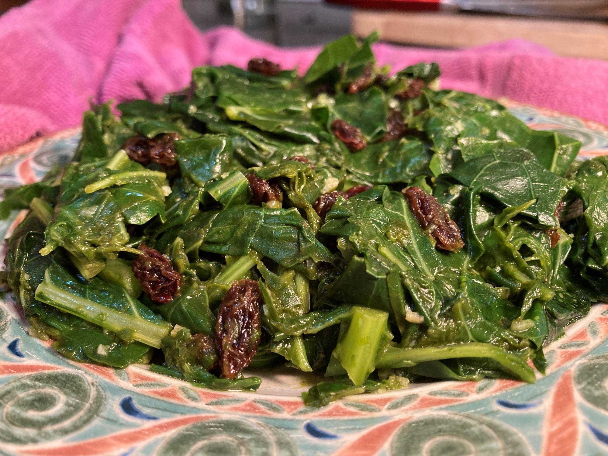 Collard greens mixed with raisins and on a colorful patterned plate with a pink towel in the background.
