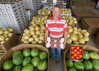 Farmer standing among his produce and holding a flat of cherry tomatoes