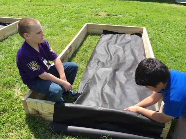 Students line a raised bed with fabric to prevent weeds from growing.