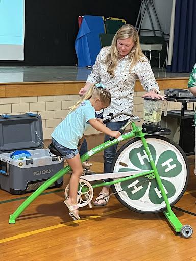 Molly Rusch assists a young child pedaling on the blender bike.