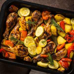 A sheet pan meal with chicken legs, squash, red bell peppers, and sprigs of rosemary.