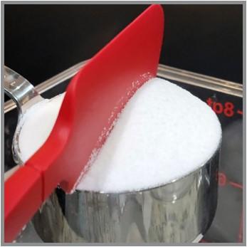 A spatula with a straight edge is being dragged across the top of the 1 cup measure, where the excess sugar is falling back into the sugar container.
