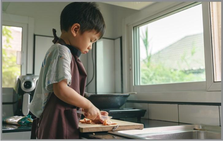 Little boy cutting sausage with a plastic knife