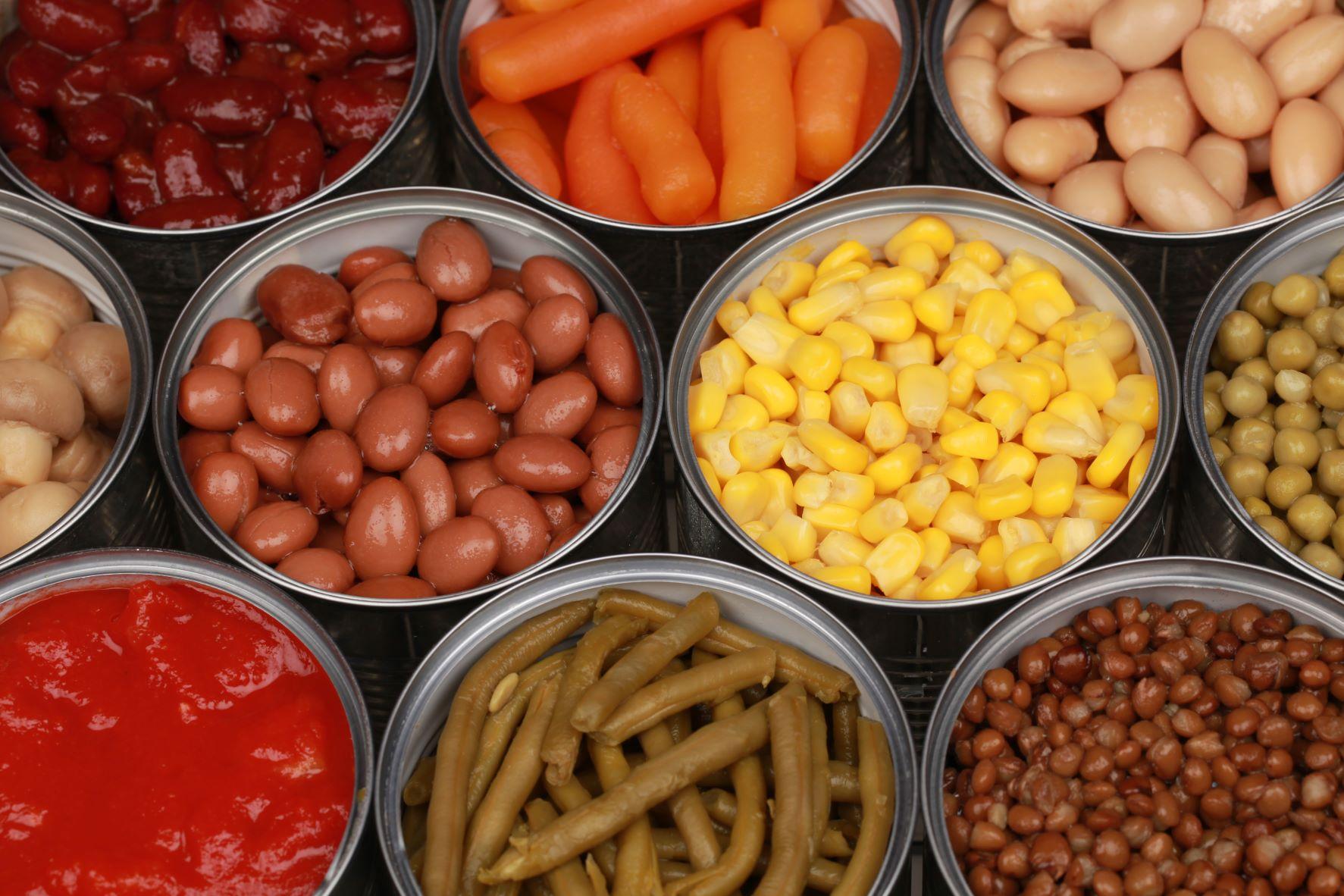 A variety of canned foods with the top off - pinto beans, carrots, corn, green beans, and northern beans.