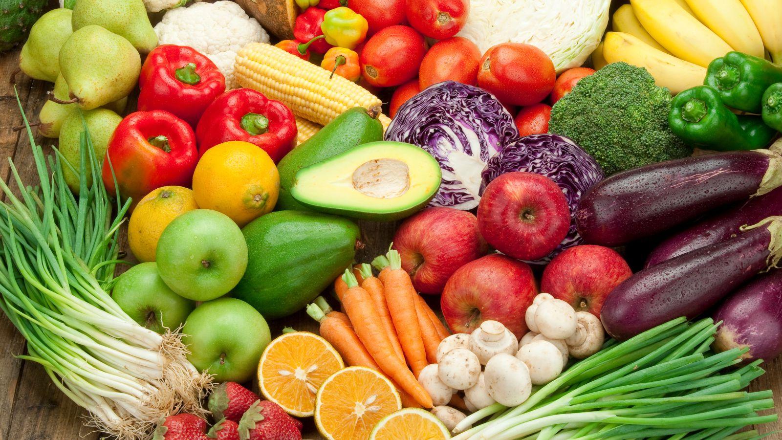 A variety of colorful fruits and vegetables including apples, peppers, carrots, onions, eggplant, tomatoes, mushrooms, and red cabbage.