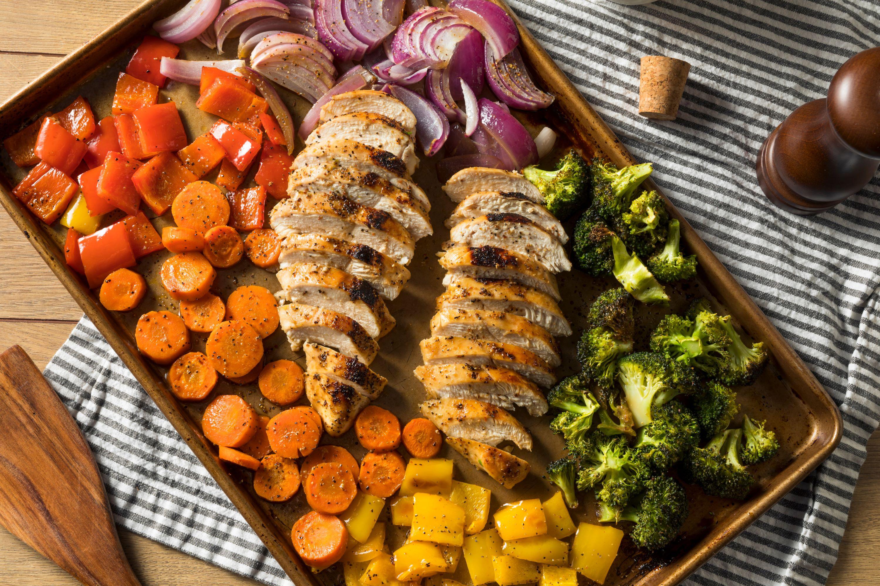 A sheet pan meal with carrots, bell peppers, broccoli, onions and chicken.