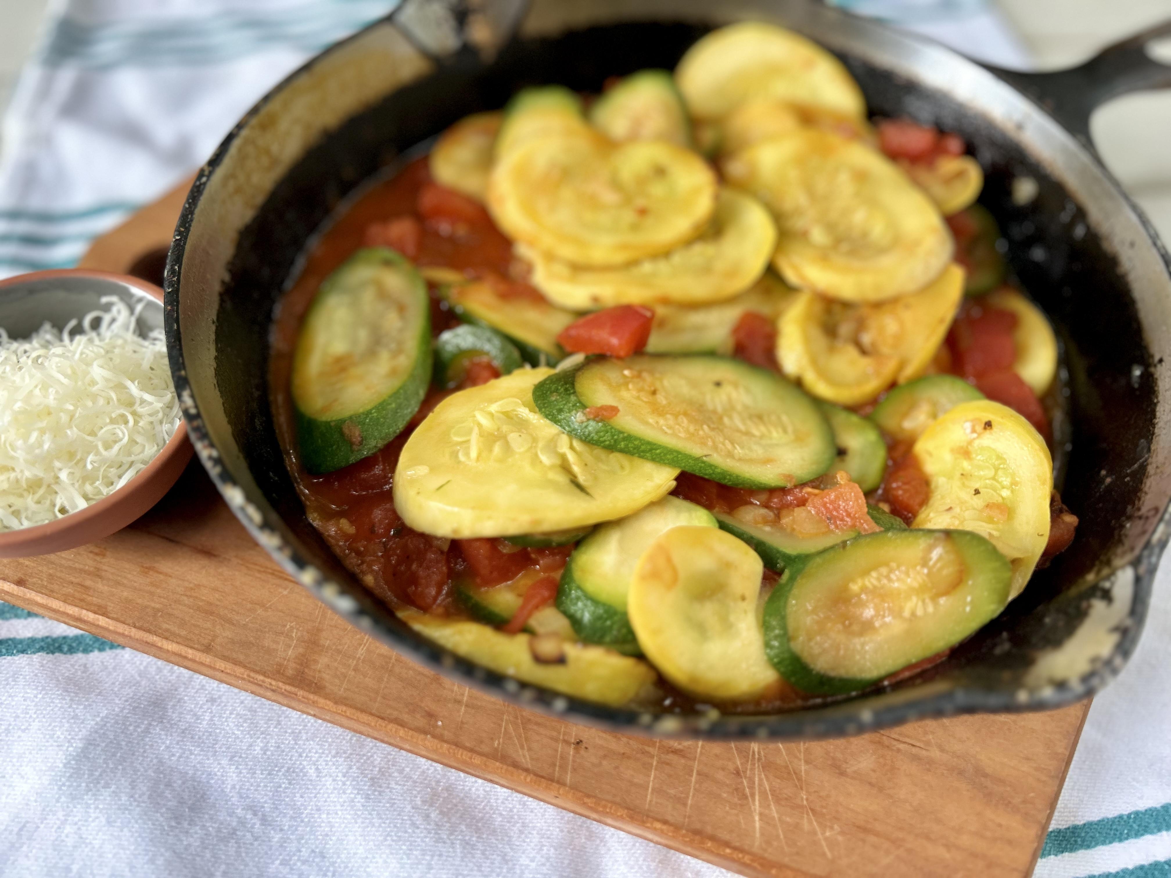 Sliced squash, zucchini, tomatoes, and onion in an iron skillet.  