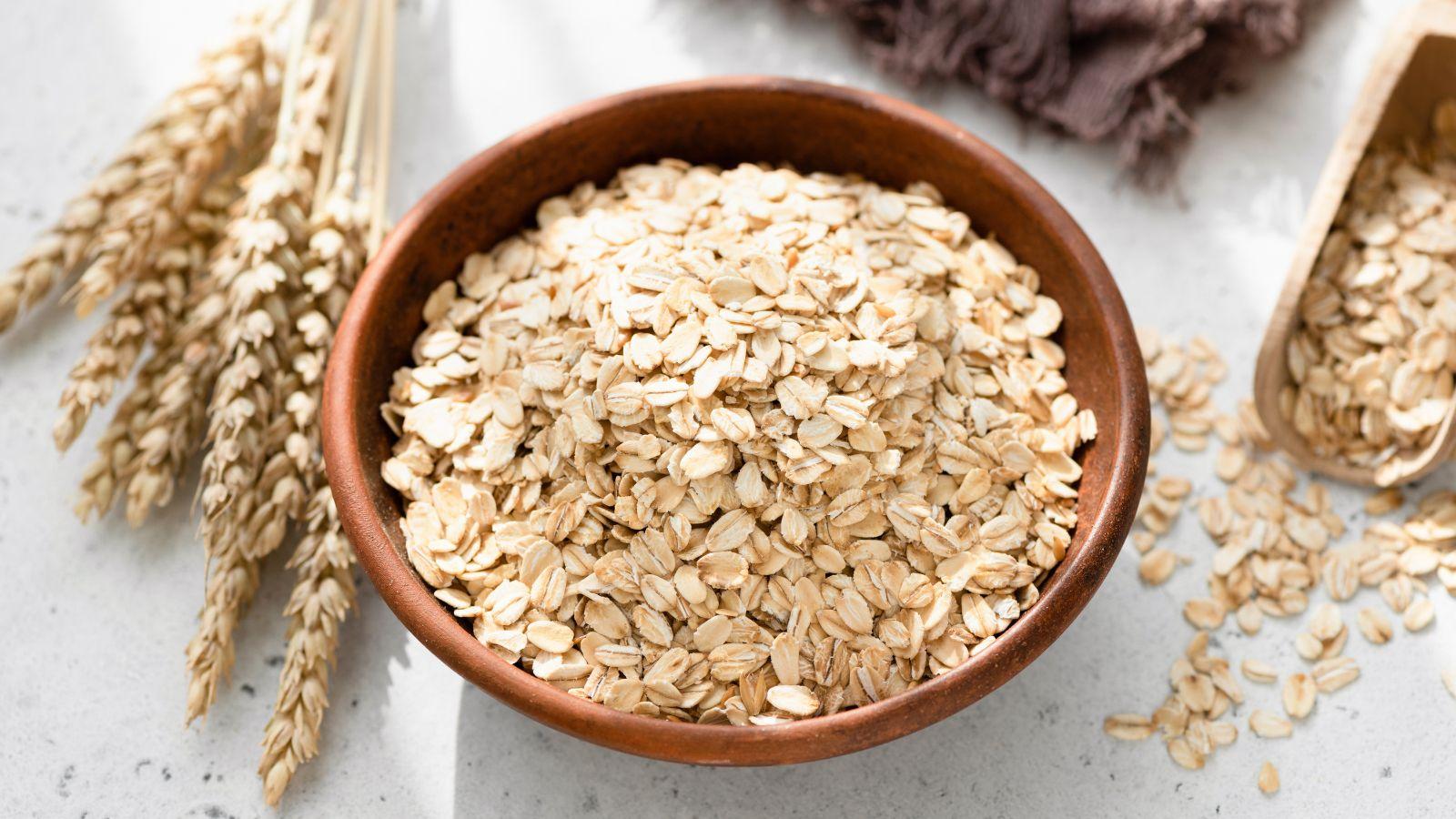 A bowl of oats surrounded by pieces of oats and a whole oat stalk.
