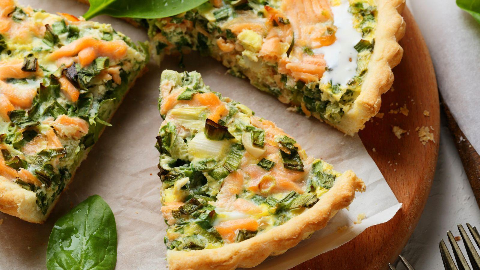 A quiche with leafy greens and tomatoes cut into three pieces.